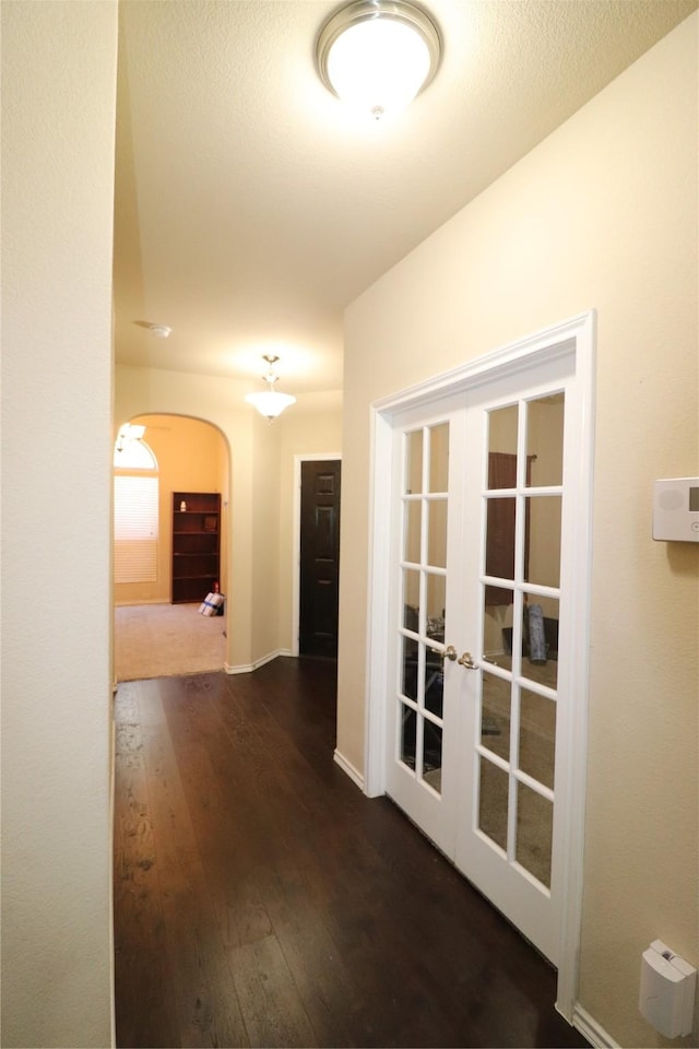 hallway featuring baseboards, arched walkways, hardwood / wood-style floors, and french doors