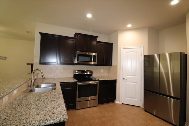 kitchen featuring tasteful backsplash, appliances with stainless steel finishes, light stone counters, and a sink