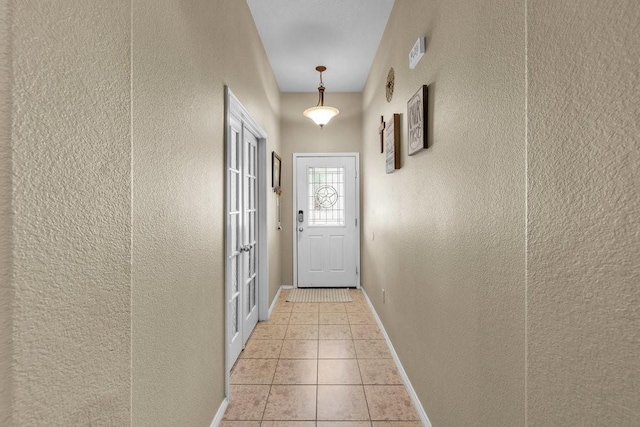 doorway to outside with a textured wall, light tile patterned flooring, and baseboards