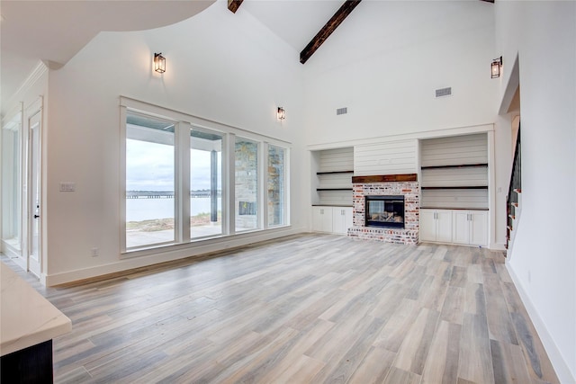 unfurnished living room with a water view, a brick fireplace, light wood-type flooring, and beamed ceiling