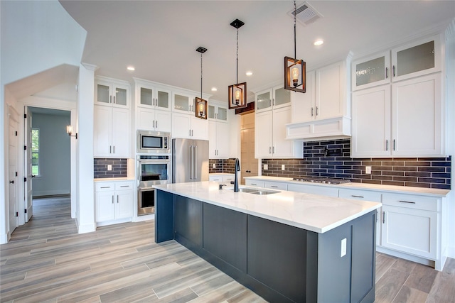 kitchen featuring glass insert cabinets, a sink, light countertops, appliances with stainless steel finishes, and a center island with sink