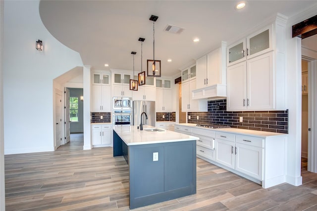 kitchen featuring an island with sink, glass insert cabinets, stainless steel appliances, and light countertops