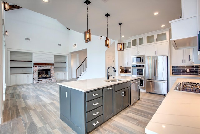 kitchen featuring white cabinets, glass insert cabinets, hanging light fixtures, stainless steel appliances, and a sink