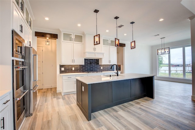 kitchen with an island with sink, glass insert cabinets, light countertops, and decorative light fixtures