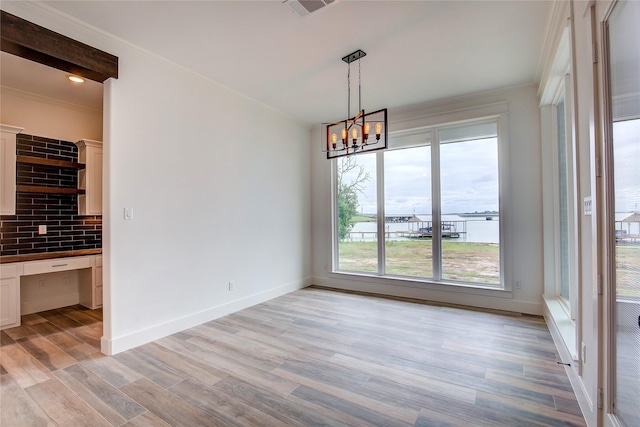 unfurnished dining area featuring baseboards, visible vents, light wood-style flooring, ornamental molding, and built in desk