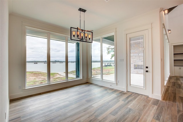 unfurnished dining area with a water view, ornamental molding, wood finished floors, a chandelier, and baseboards