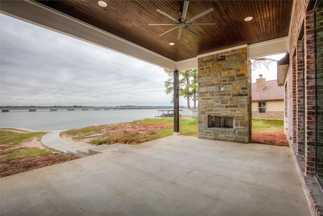 view of patio with a water view, ceiling fan, and an outdoor stone fireplace