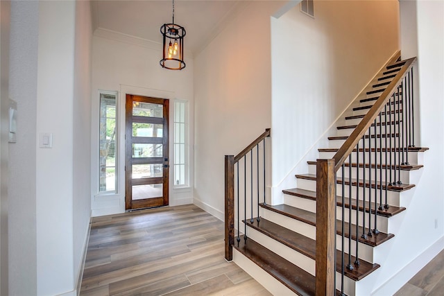 foyer featuring wood finished floors, visible vents, baseboards, stairs, and crown molding