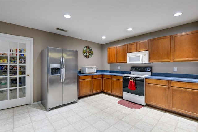 kitchen with white appliances, visible vents, brown cabinetry, and light floors