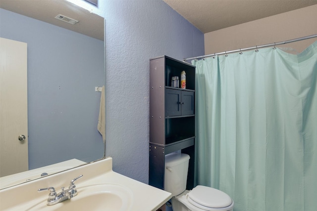 bathroom with toilet, a textured wall, visible vents, and vanity