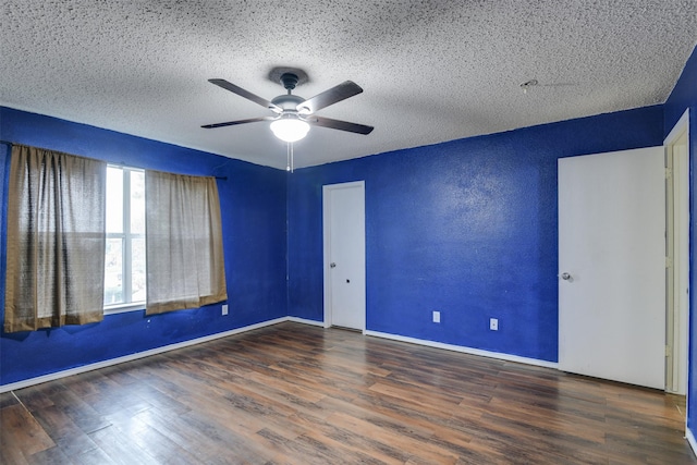 spare room with baseboards, a ceiling fan, a textured wall, dark wood-type flooring, and a textured ceiling