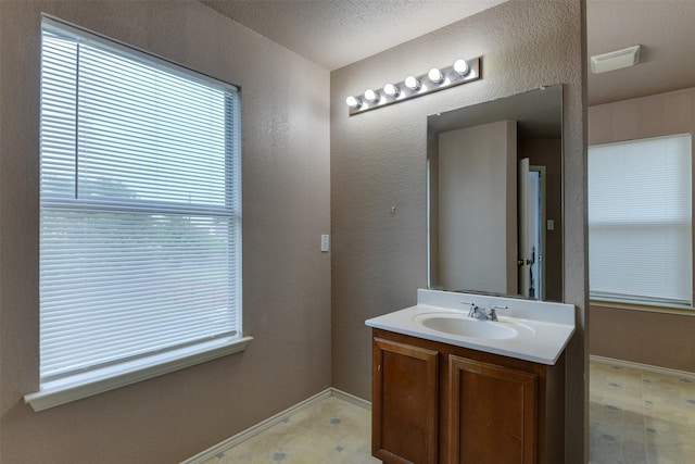 bathroom with visible vents, a textured wall, vanity, baseboards, and tile patterned floors