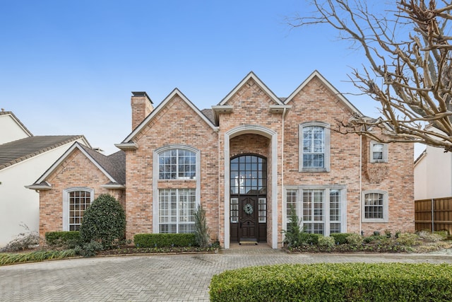 traditional home featuring brick siding, a chimney, and fence