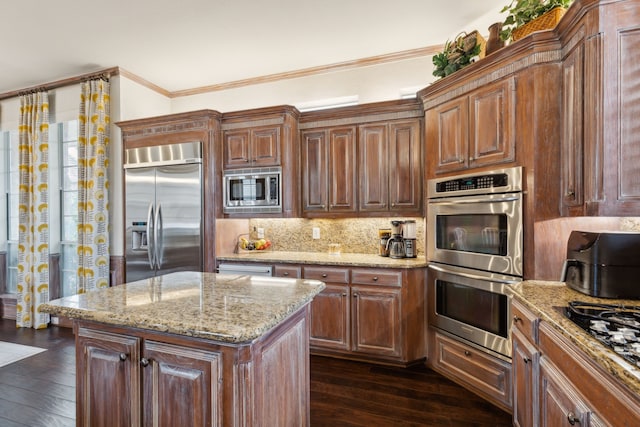 kitchen featuring built in appliances, ornamental molding, a center island, dark wood-style floors, and tasteful backsplash