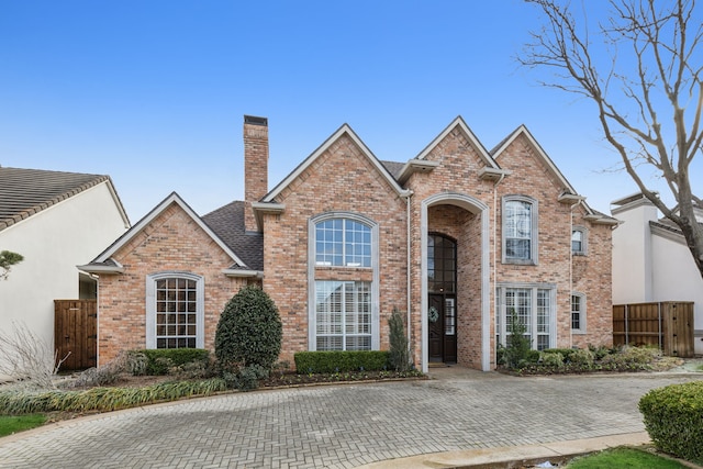 traditional home featuring a shingled roof, brick siding, fence, and a chimney