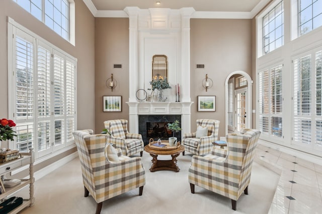 living room with a high ceiling, a healthy amount of sunlight, a high end fireplace, and crown molding