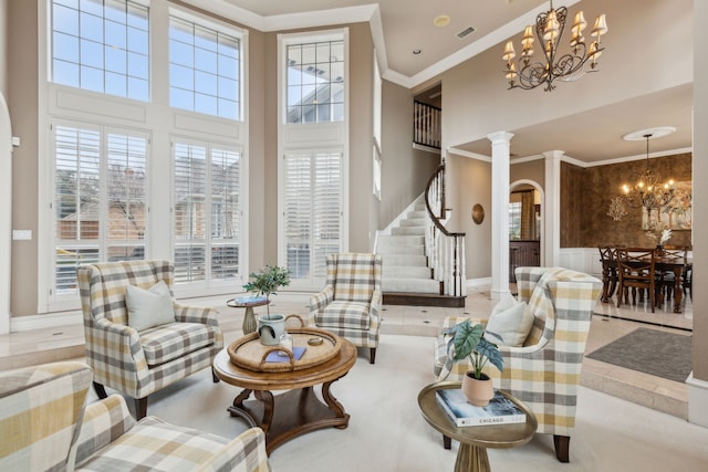 living area featuring a healthy amount of sunlight, ornate columns, crown molding, and a notable chandelier