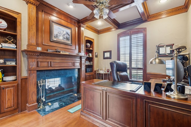 home office with built in shelves, a premium fireplace, a ceiling fan, light wood-type flooring, and coffered ceiling