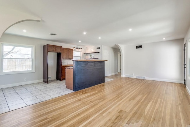 kitchen featuring baseboards, a center island, arched walkways, open floor plan, and decorative backsplash
