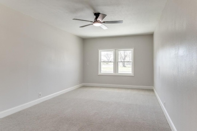spare room featuring light colored carpet, ceiling fan, and baseboards