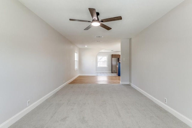 spare room featuring ceiling fan, arched walkways, light carpet, and baseboards