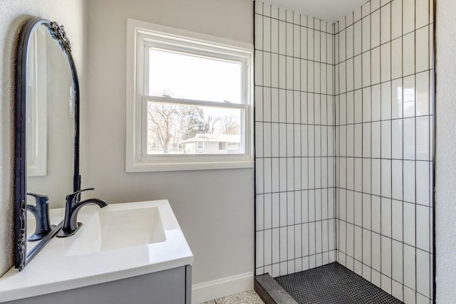bathroom with tiled shower, vanity, and baseboards