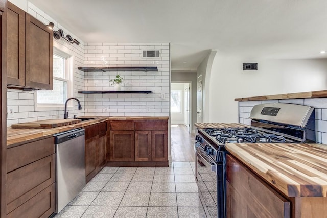 kitchen featuring tasteful backsplash, butcher block countertops, visible vents, stainless steel appliances, and a sink