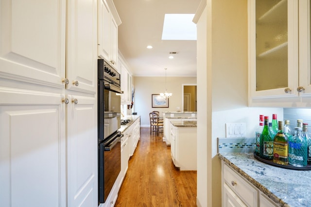 kitchen with pendant lighting, glass insert cabinets, white cabinetry, light stone countertops, and light wood-type flooring