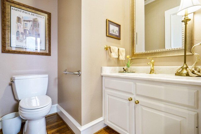 half bath with vanity, wood finished floors, toilet, and baseboards