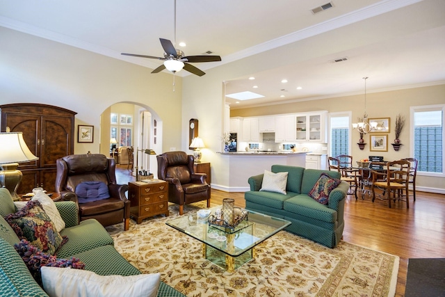 living area featuring arched walkways, wood finished floors, visible vents, baseboards, and ornamental molding