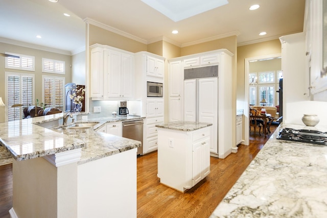 kitchen featuring built in appliances, a peninsula, a center island, white cabinetry, and a sink