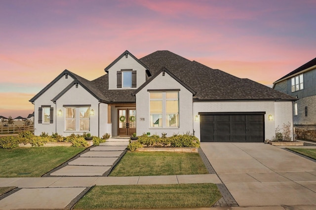 view of front of property with an attached garage, driveway, a lawn, roof with shingles, and stucco siding