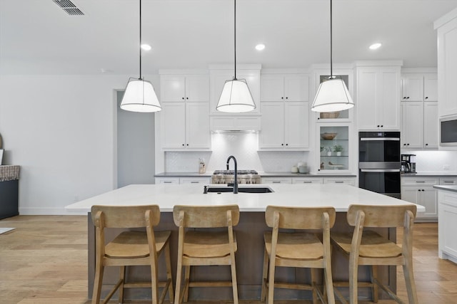 kitchen with tasteful backsplash, visible vents, multiple ovens, light wood-style floors, and white cabinetry