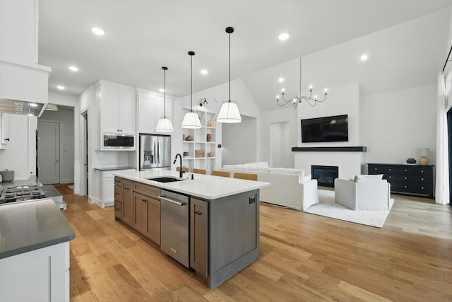 kitchen featuring white cabinets, a glass covered fireplace, appliances with stainless steel finishes, light wood-type flooring, and a sink