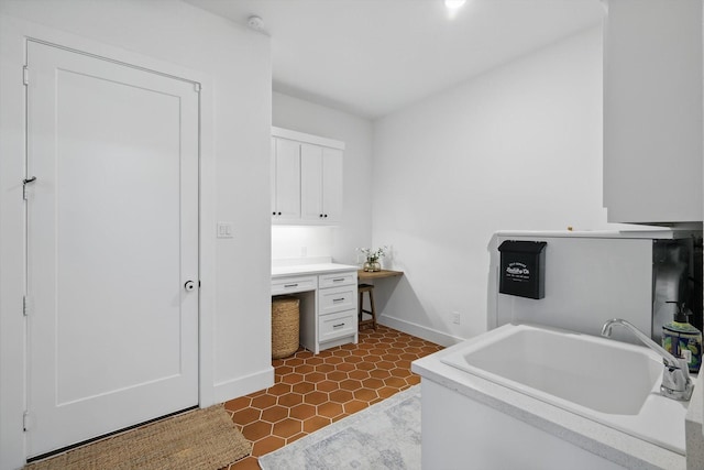 interior space featuring baseboards, built in desk, a sink, and white cabinets