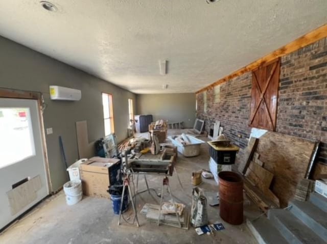 living area featuring a textured ceiling, brick wall, a wall mounted AC, and unfinished concrete flooring