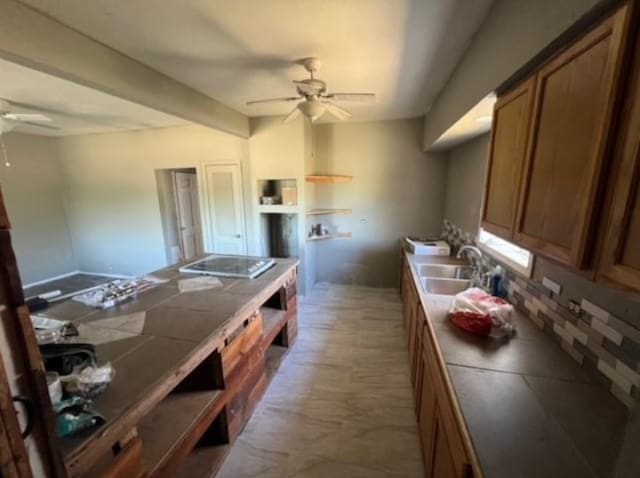 kitchen with black electric stovetop, a sink, a ceiling fan, tile counters, and brown cabinets