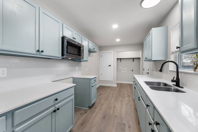 kitchen featuring stainless steel microwave, light countertops, light wood-type flooring, a sink, and recessed lighting