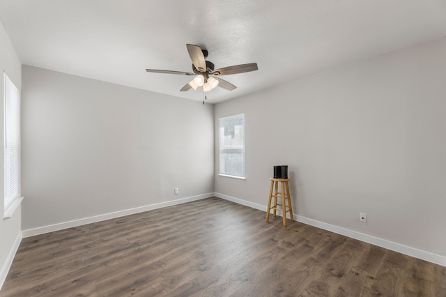 empty room with ceiling fan, dark wood finished floors, and baseboards