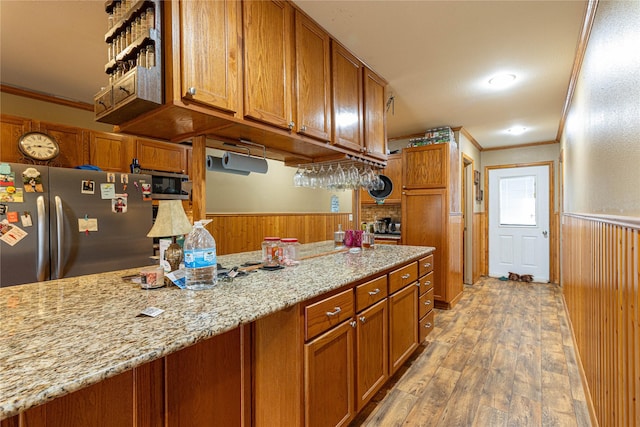 kitchen featuring light stone countertops, a wainscoted wall, brown cabinets, and freestanding refrigerator