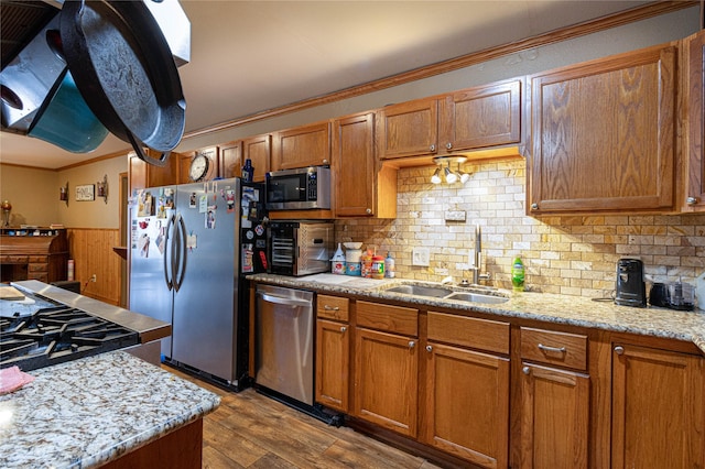 kitchen with wood finished floors, a sink, ornamental molding, appliances with stainless steel finishes, and brown cabinetry