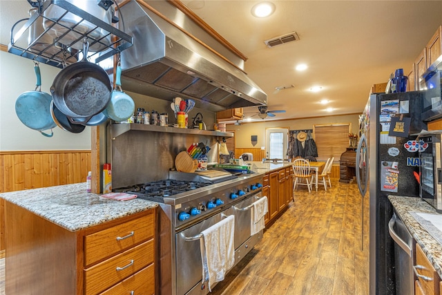 kitchen with visible vents, wainscoting, appliances with stainless steel finishes, wood finished floors, and ventilation hood