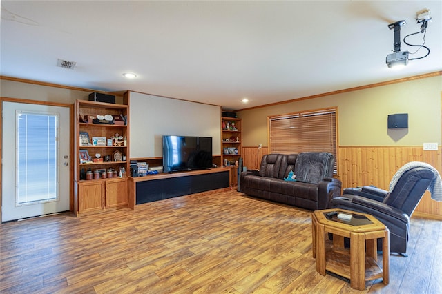 living room featuring wood walls, wood finished floors, visible vents, wainscoting, and crown molding