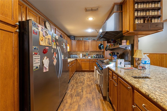 kitchen with light stone counters, brown cabinets, stainless steel appliances, visible vents, and island range hood