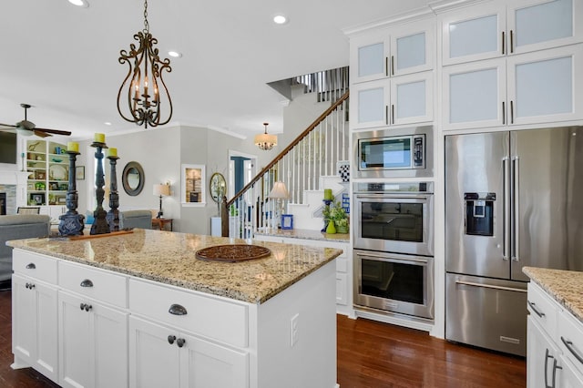 kitchen with a center island, decorative light fixtures, stainless steel appliances, a stone fireplace, and white cabinetry