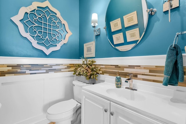 bathroom featuring tile walls, wainscoting, vanity, and toilet