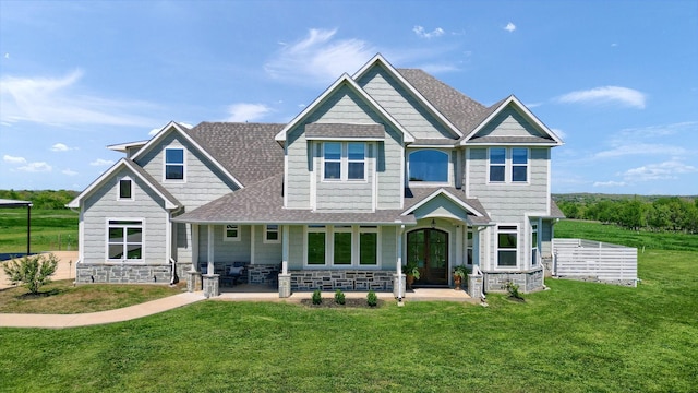 craftsman house featuring a shingled roof, stone siding, and a front lawn