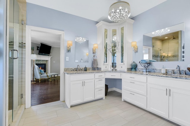 full bath with a notable chandelier, a sink, a shower stall, double vanity, and a glass covered fireplace