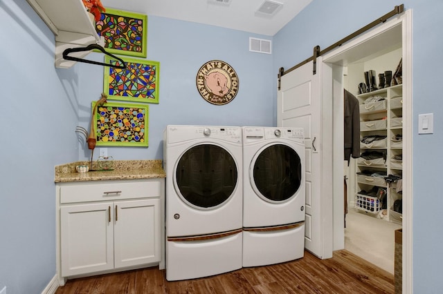 clothes washing area featuring a barn door, independent washer and dryer, wood finished floors, and visible vents