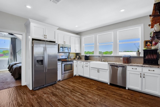 kitchen with stainless steel appliances, a sink, white cabinets, light stone countertops, and tasteful backsplash